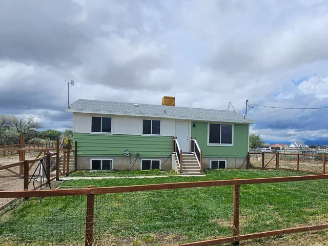 Split-level residence featuring a light green and white exterior, an accessible front yard with a wooden fence, and an expansive side yard