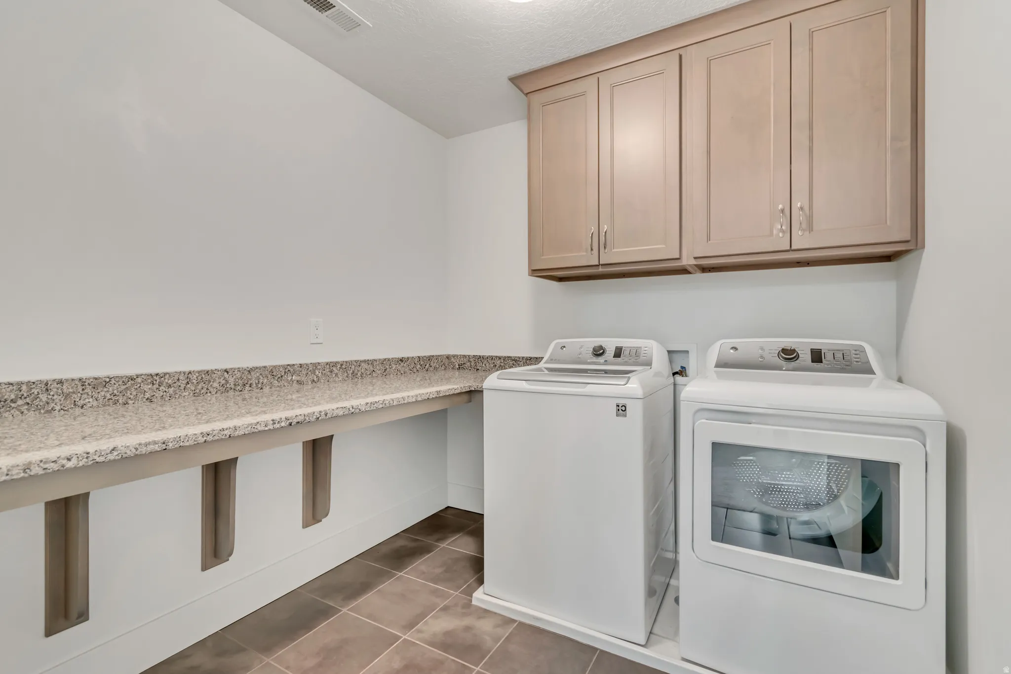 Laundry area featuring upper cabinetry, a spacious countertop, and durable tile flooring