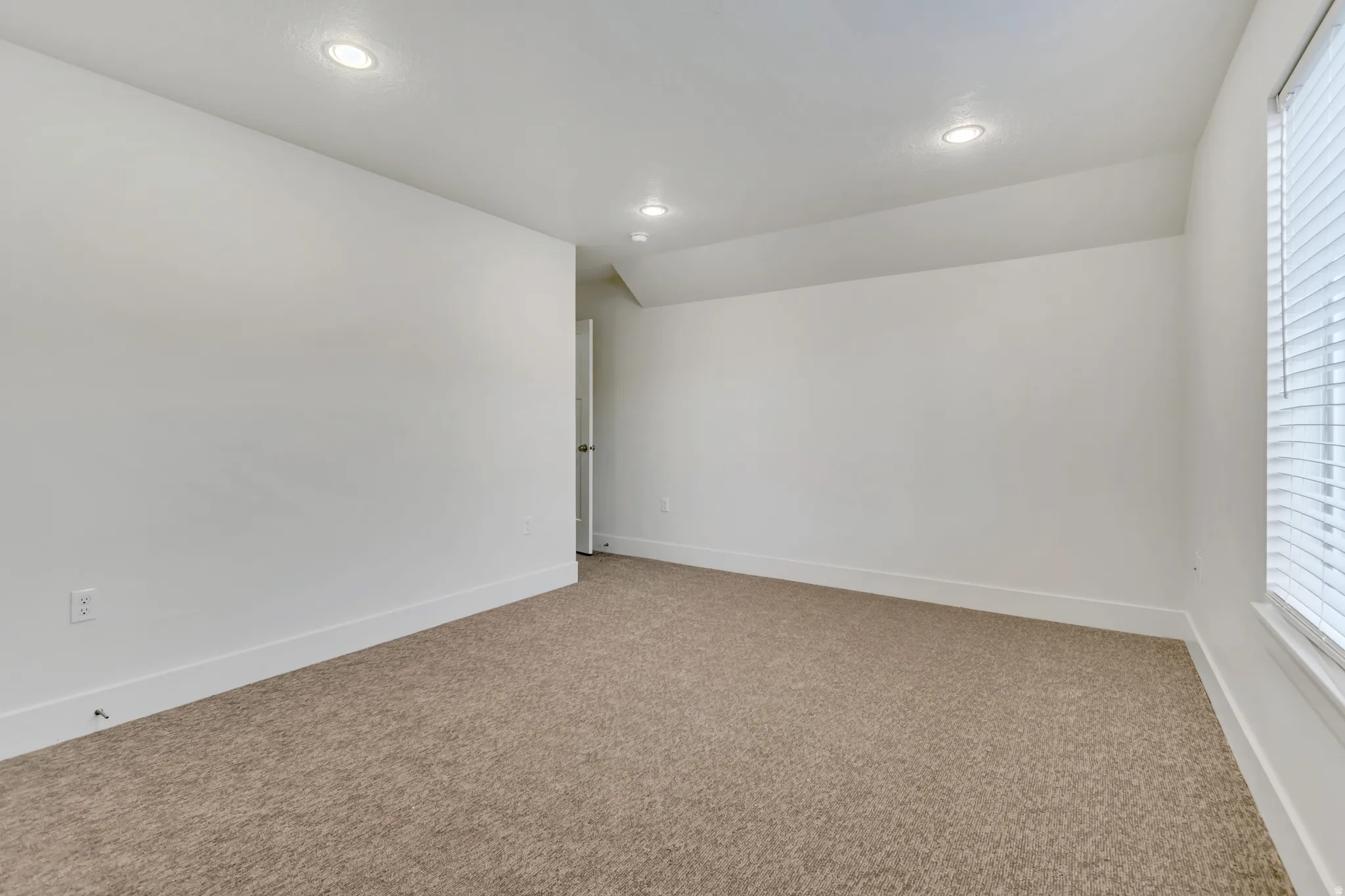 Carpeted room with recessed lighting, white walls, and a window with horizontal blinds