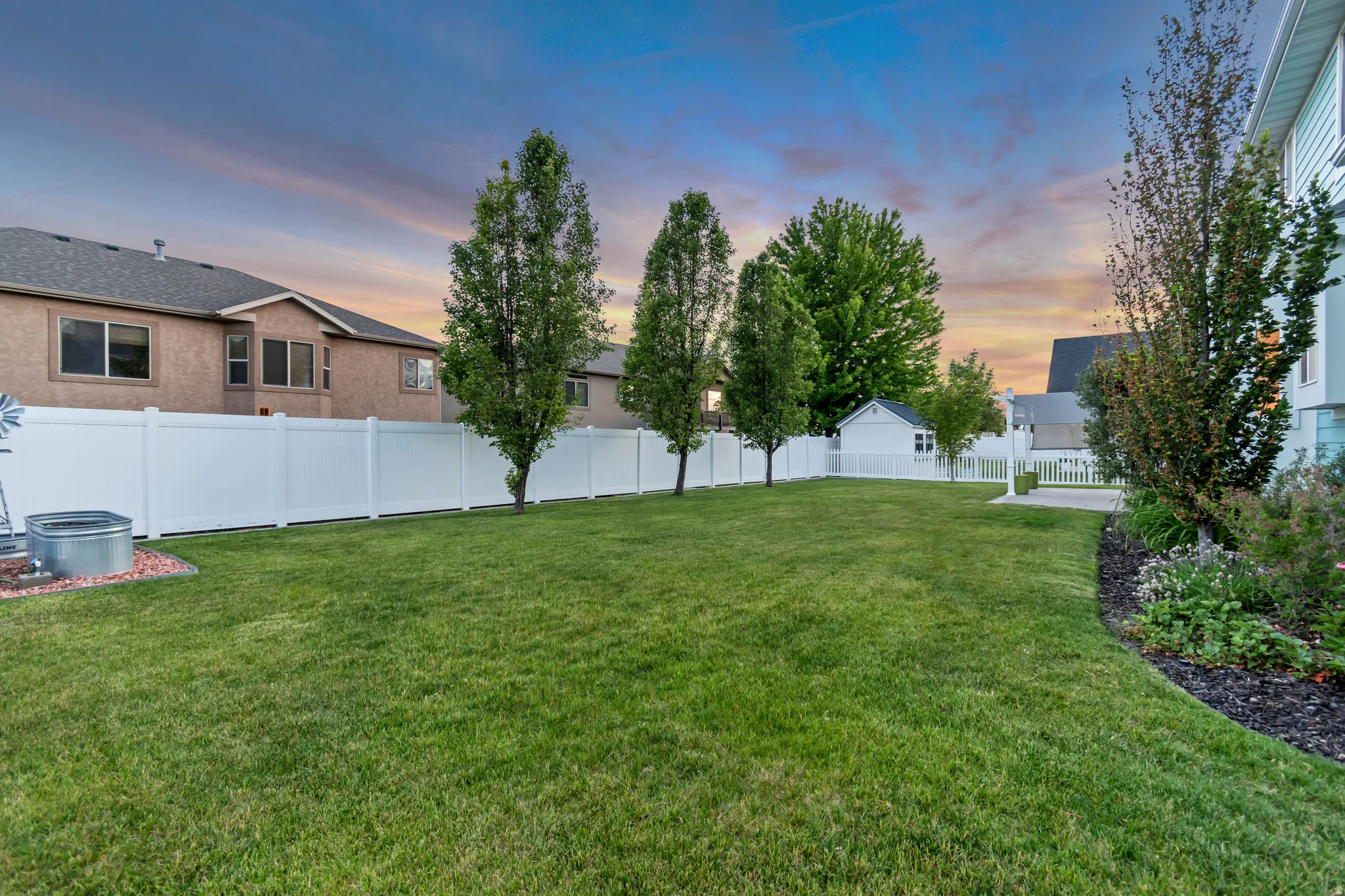 Expansive lawn area featuring a white privacy fence and mature trees