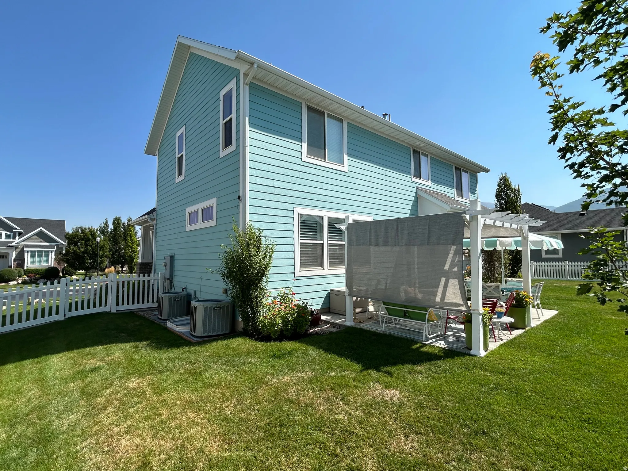 Rear exterior featuring light blue siding, a white pergola with a shade cover, and a white picket fence enclosing a portion of the yard