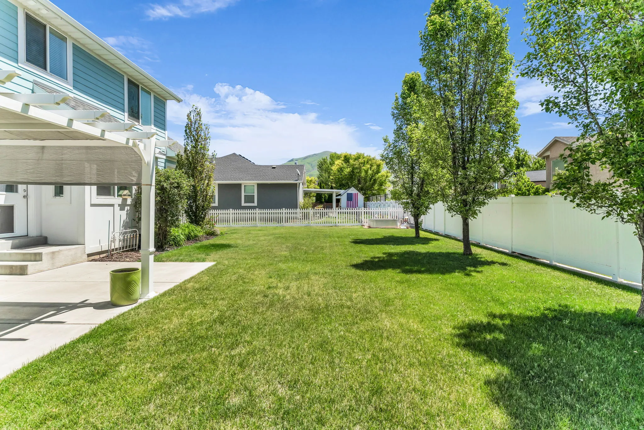 Expansive green lawn with mature trees and a white vinyl privacy fence