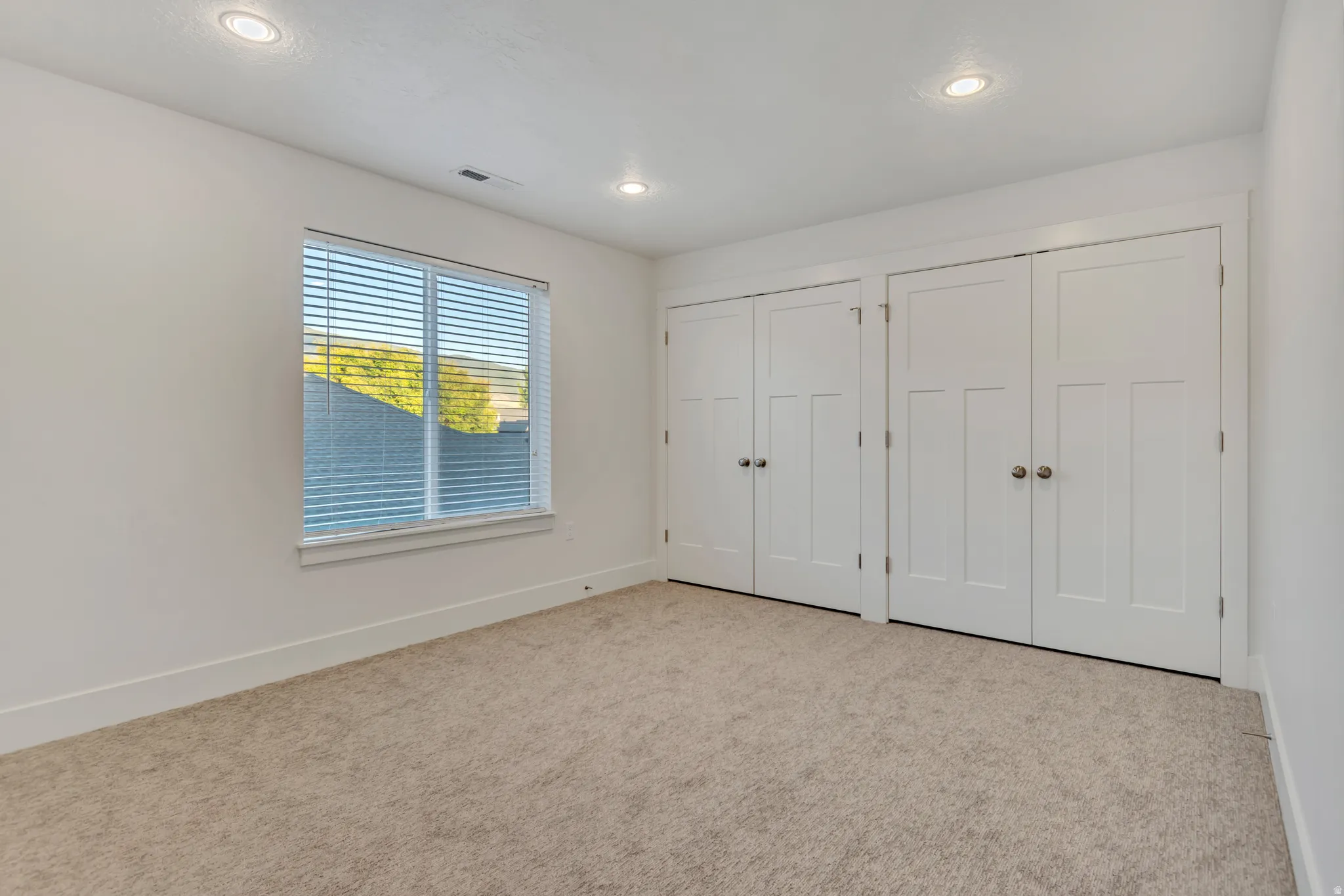 Room featuring wall-to-wall carpeting, a large window with horizontal blinds, recessed ceiling lighting, and two sets of bi-fold closet doors