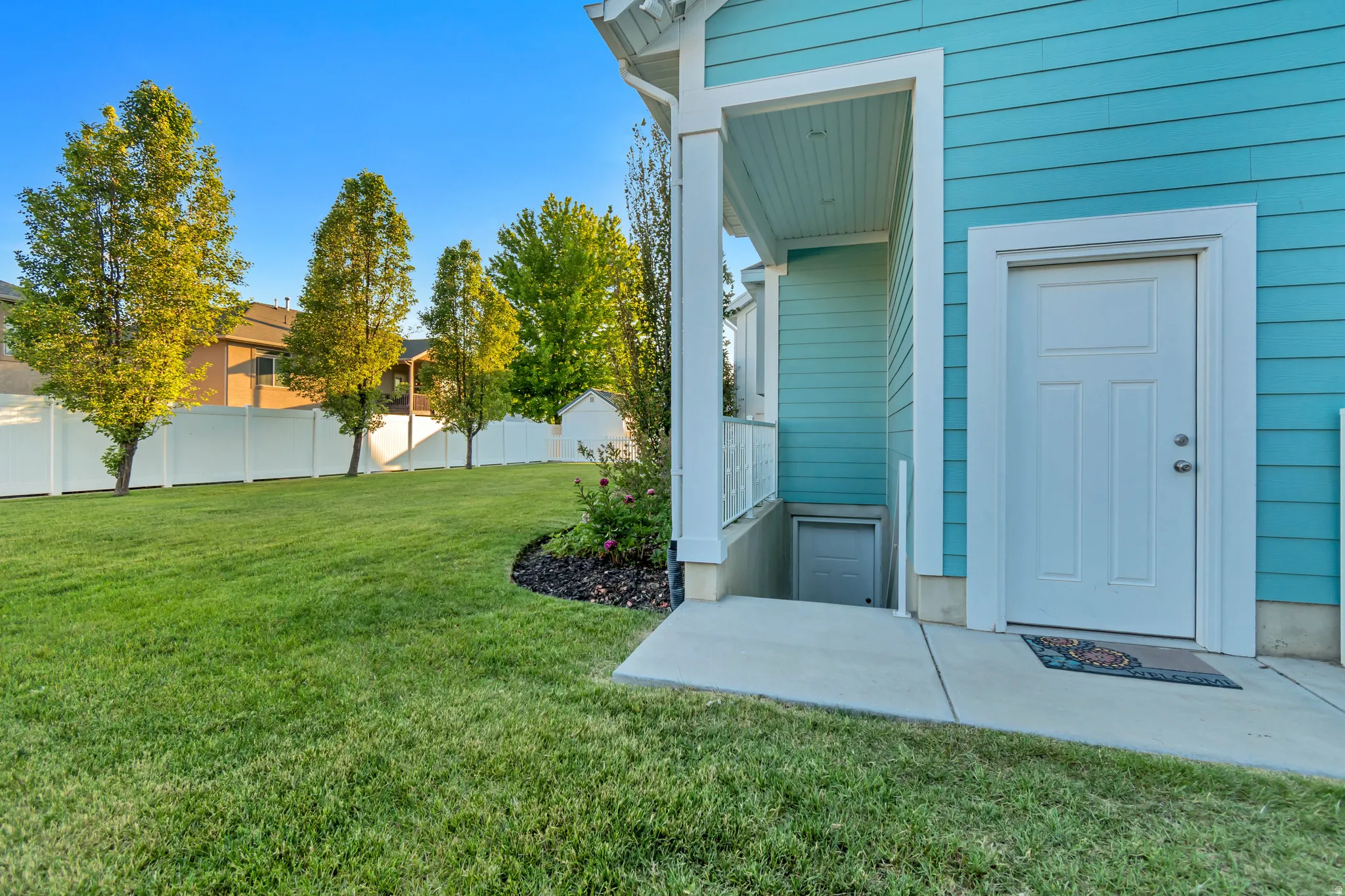Expansive green lawn with a white vinyl fence and mature trees