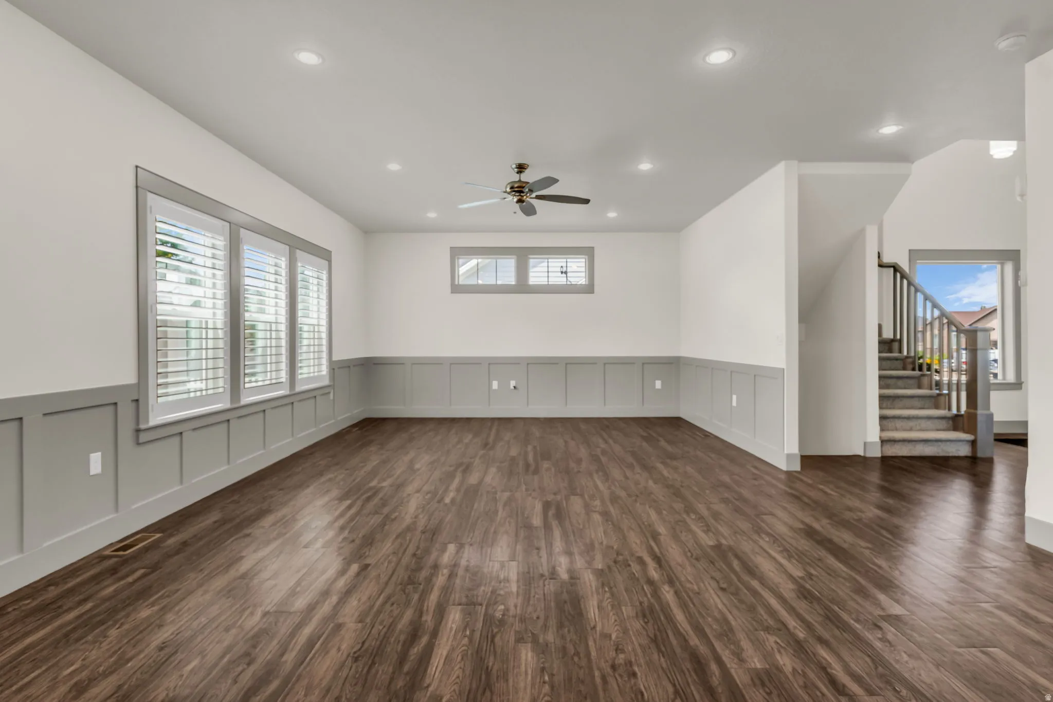 Spacious interior featuring wood-finish flooring, wainscoting, recessed lighting, a ceiling fan, and a carpeted staircase with a wood railing