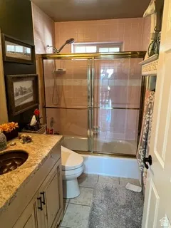 Bathroom featuring a vanity with an integrated sink, a toilet, and a combination tub and shower with a gold-toned framed glass enclosure