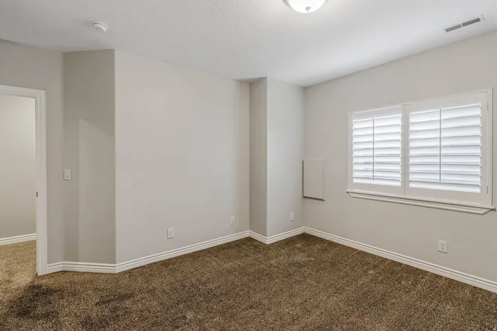 Carpeted room featuring a double window with white plantation shutters, light gray wall paint, and white trim molding