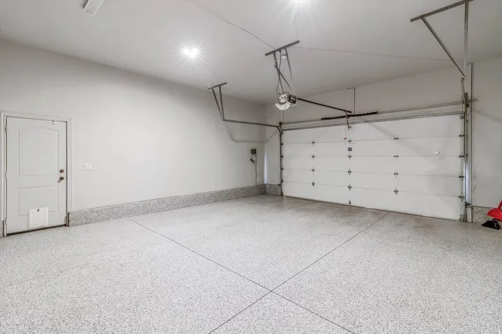 Attached garage with a speckled epoxy floor, white interior door, and overhead garage door opener system