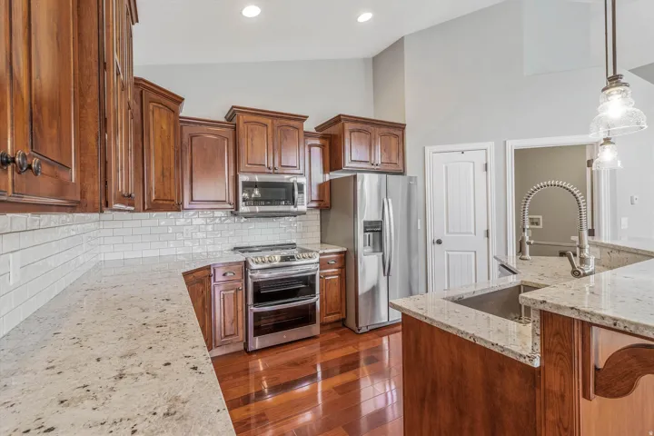 Kitchen featuring rich wood cabinetry, stainless steel appliances, speckled countertops, a white subway tile backsplash, and wood-finish flooring