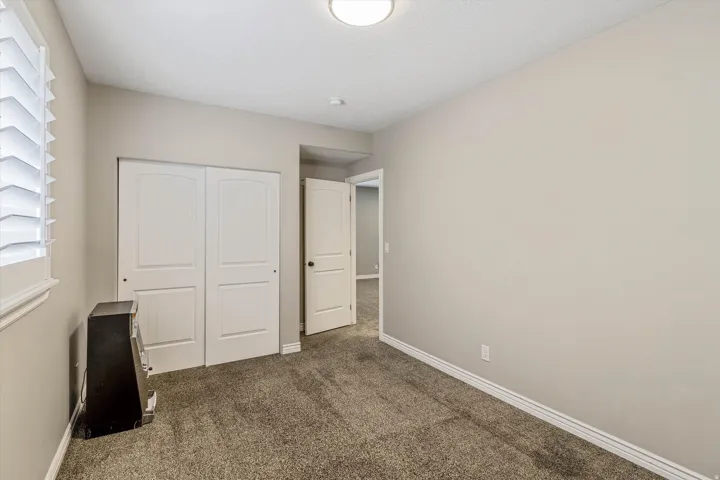 Neutral-toned room featuring plush carpeting, white baseboards, a window with plantation shutters, and a closet with white bi-fold doors
