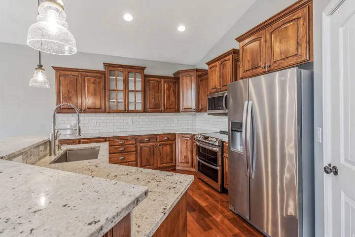 Spacious kitchen featuring a peninsula with granite countertops, stainless steel appliances, wood cabinetry, and a subway tile backsplash