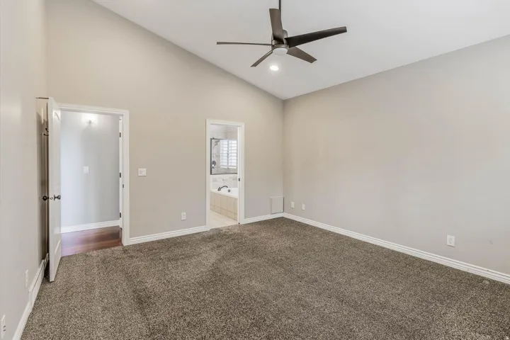Spacious room featuring vaulted ceilings, a ceiling fan with integrated lighting, and neutral-toned carpet flooring
