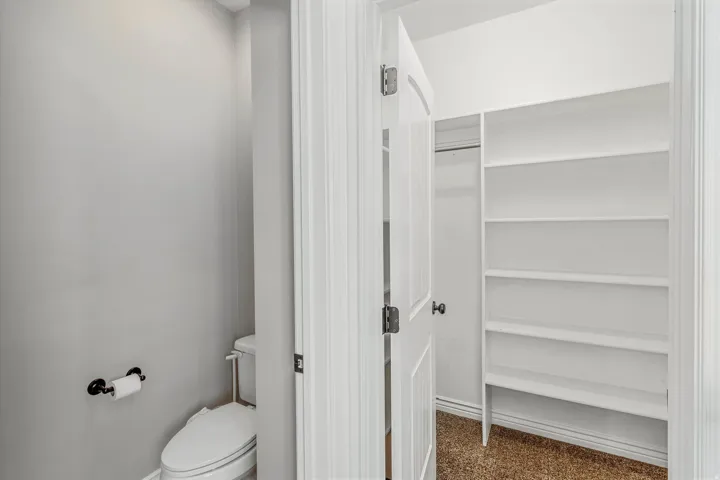 Recessed closet featuring multiple white shelving units and a hanging rod, complemented by a white paneled door with black hardware