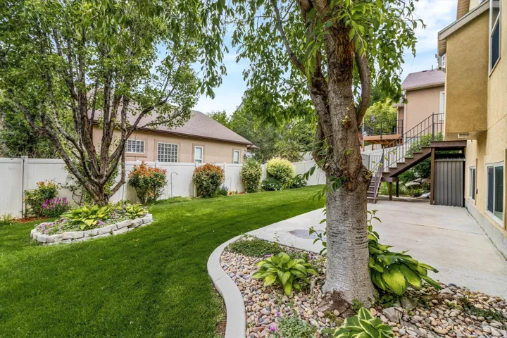 Spacious backyard featuring a manicured lawn, established trees, and a concrete patio