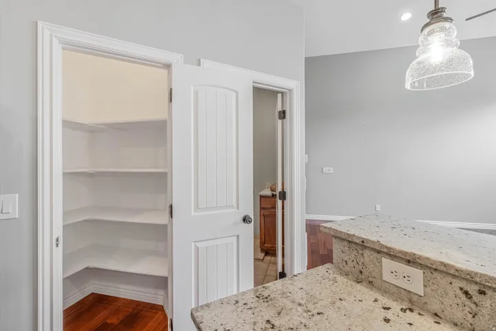 Kitchen pantry featuring multiple white shelves and wood-finish flooring