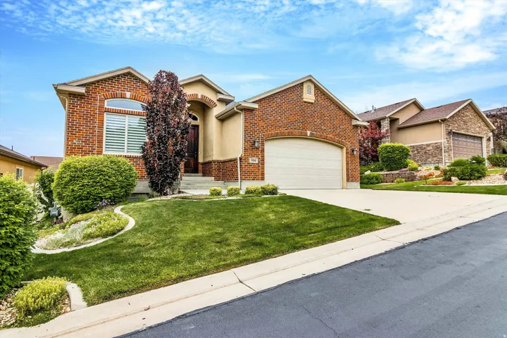 Brick and stucco exterior with an arched entry, an integrated two-car garage, and established landscaping