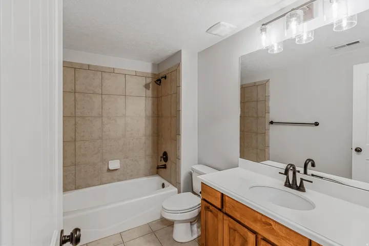 Bathroom featuring a white bathtub, tiled shower surround, wood-finish vanity, white countertop with integrated sink, and an expansive wall mirror