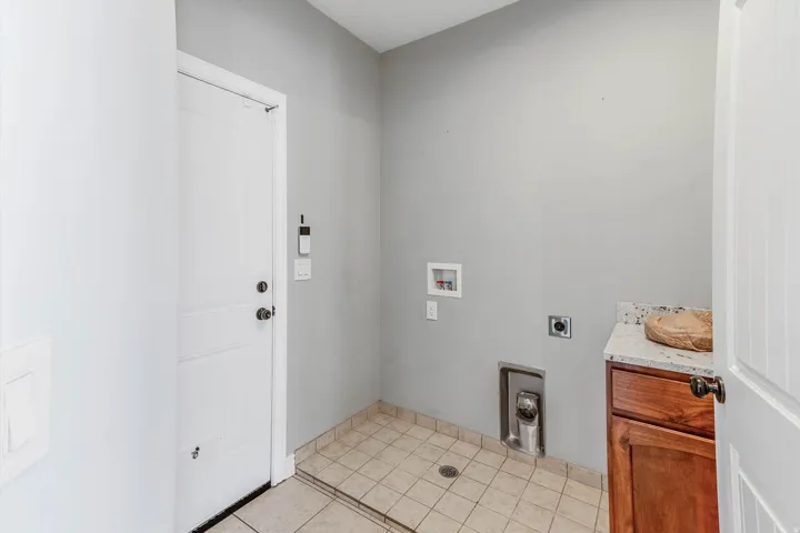 Utility area featuring light gray walls, tile flooring with a floor drain, and a wood-finish cabinet with a light-toned countertop