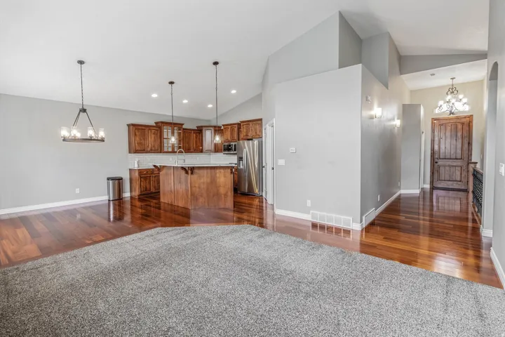 Open-concept living space featuring wood-finish flooring, a kitchen island with pendant lighting, stainless steel appliances, and a vaulted ceiling
