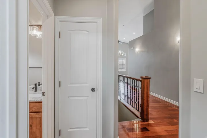 Hallway featuring wood-finish flooring, a white paneled door, and a staircase with a wood newel post and wrought iron balusters