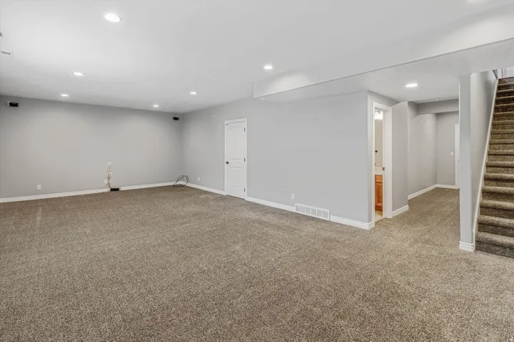 Spacious room featuring neutral carpeting, recessed lighting, light gray walls, white trim, and a carpeted staircase