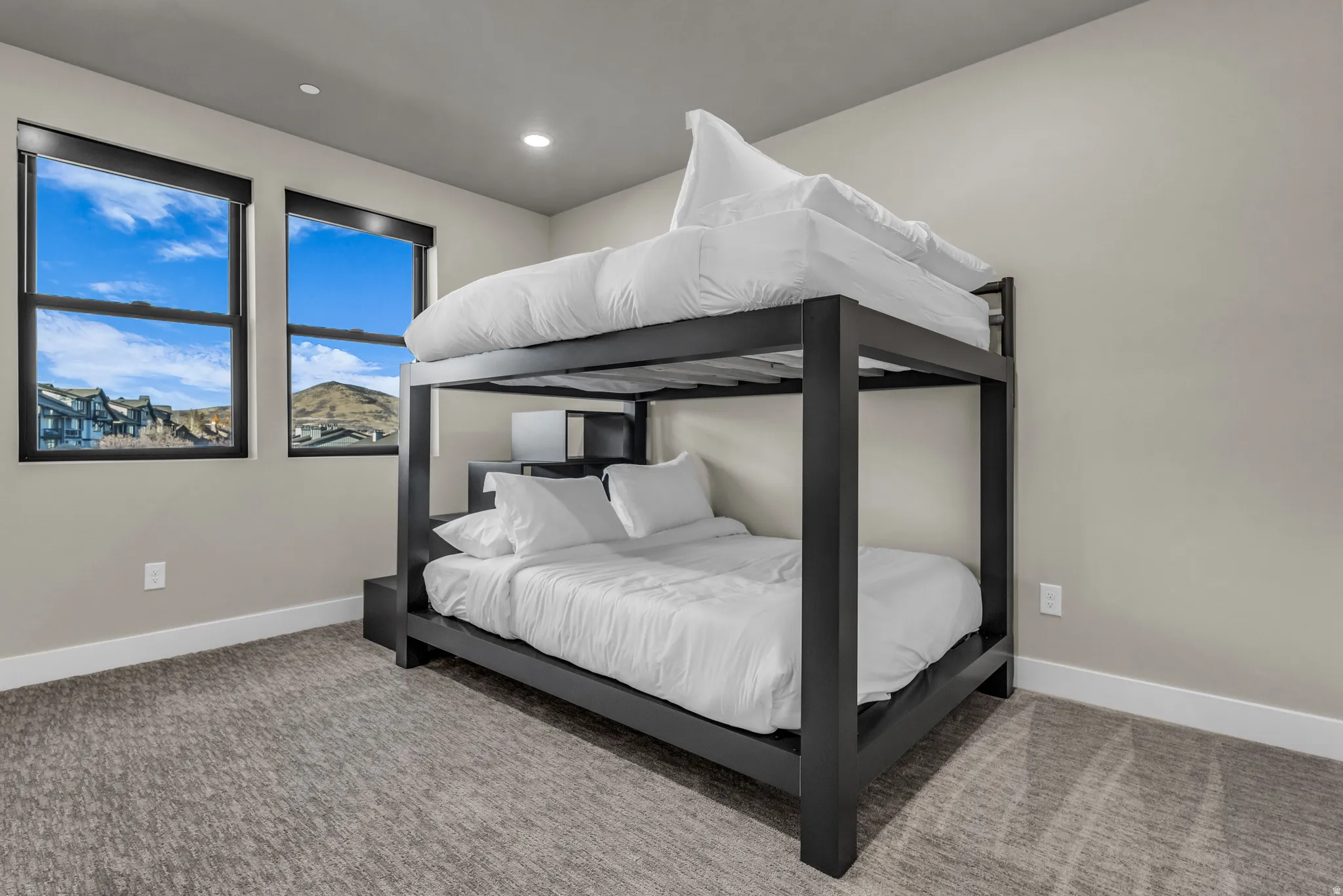Bright bedroom featuring two windows with black trim, recessed lighting, and neutral-toned carpeting