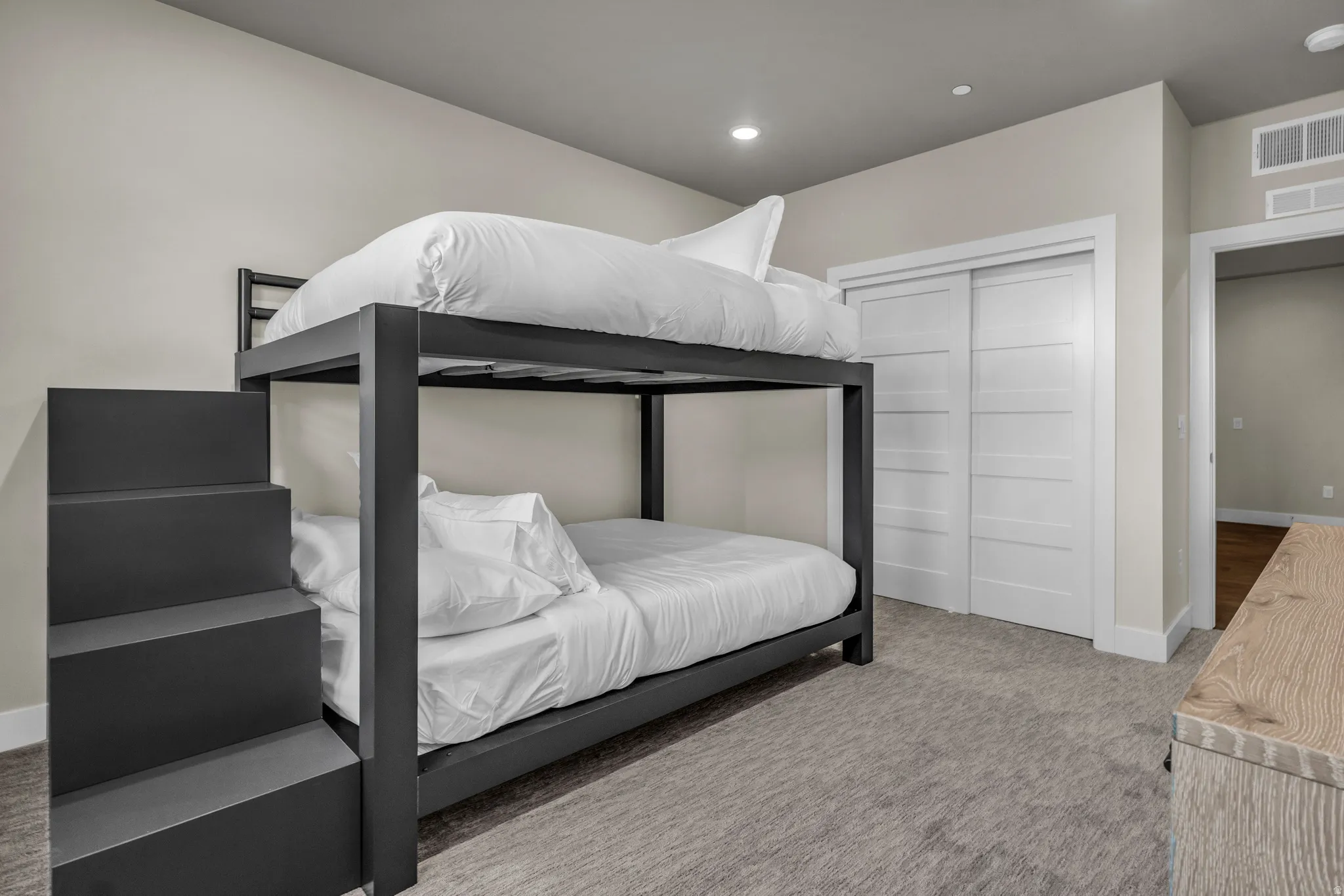 Spacious room featuring neutral-toned walls, gray carpeting, and a built-in bunk bed with stairs
