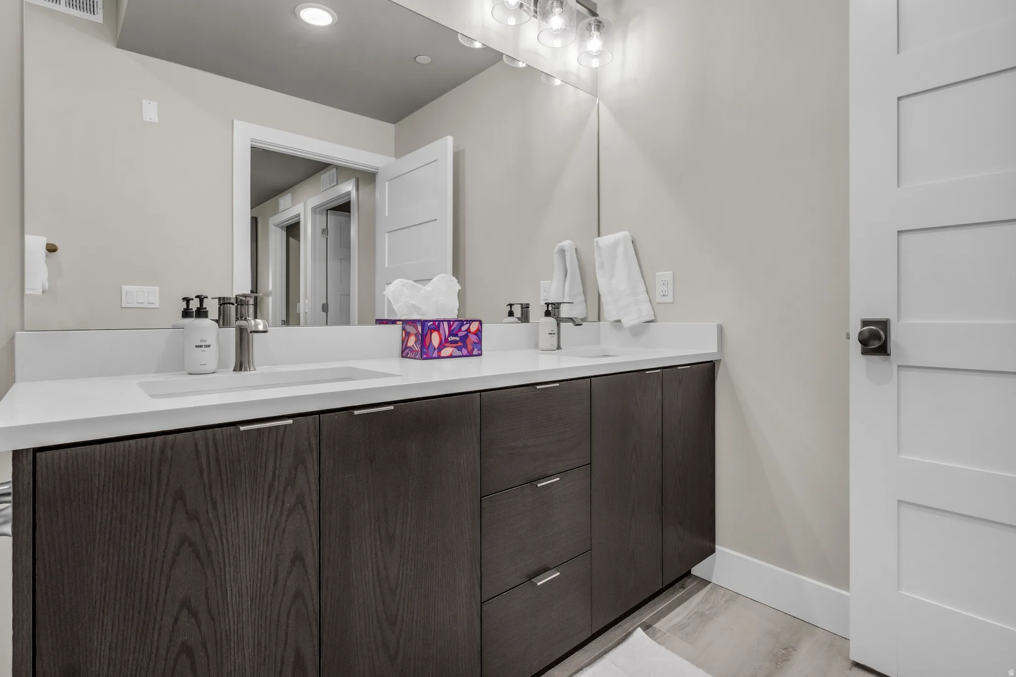 Double vanity with integrated sinks, white countertops, dark wood-finish cabinetry, and contemporary brushed nickel fixtures