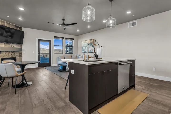 Open concept living area featuring wood-finish flooring, a kitchen island with sink and integrated dishwasher, recessed lighting, and large windows