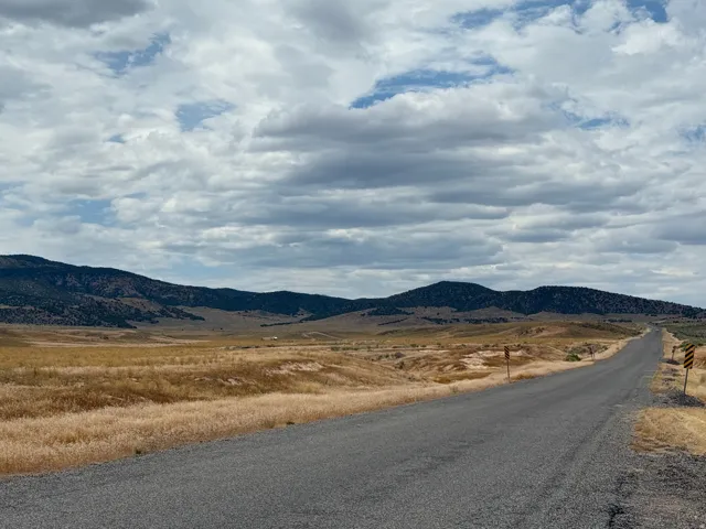 Paved road extending through expansive, dry grasslands with distant mountains