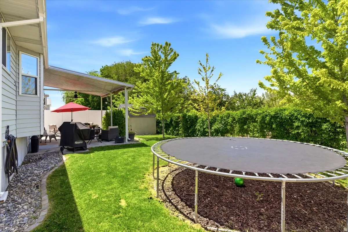 Expansive backyard featuring a covered patio, manicured lawn, and mature perimeter foliage