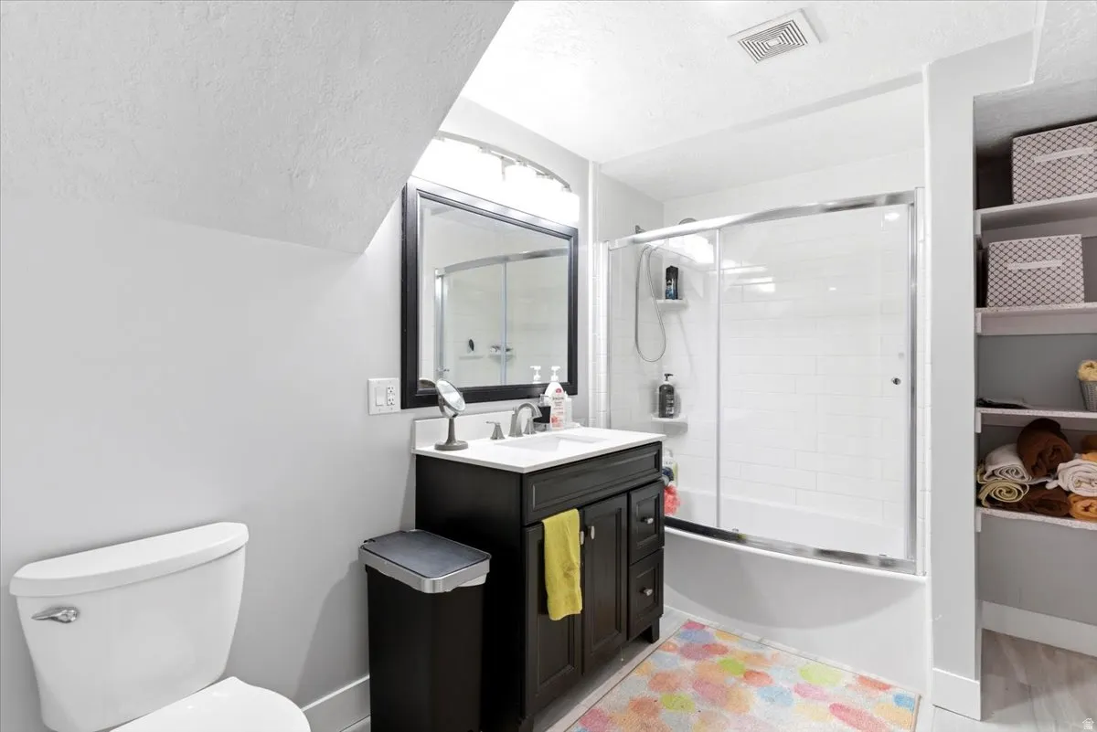 Bathroom featuring a dark wood-finish vanity with a white countertop and undermount sink, a framed mirror, and a sliding glass shower enclosure over a bathtub