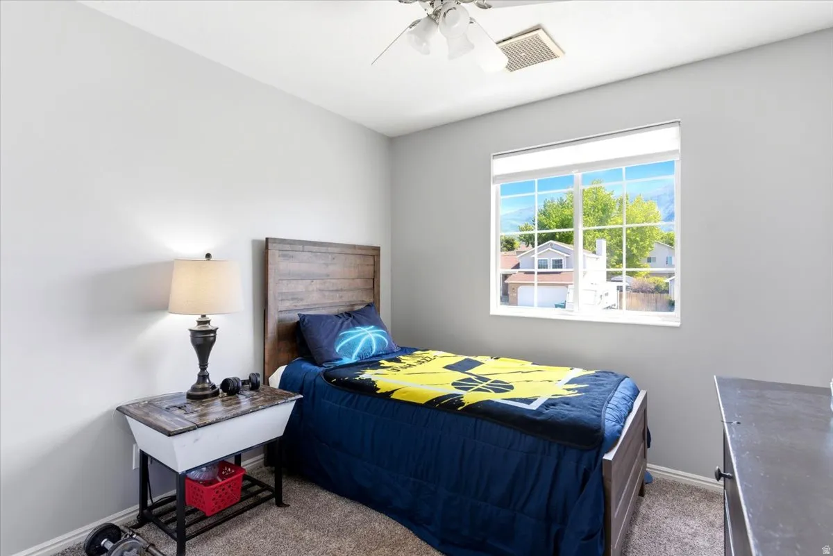 Carpeted room with light grey walls, a window with white trim, and a ceiling fan