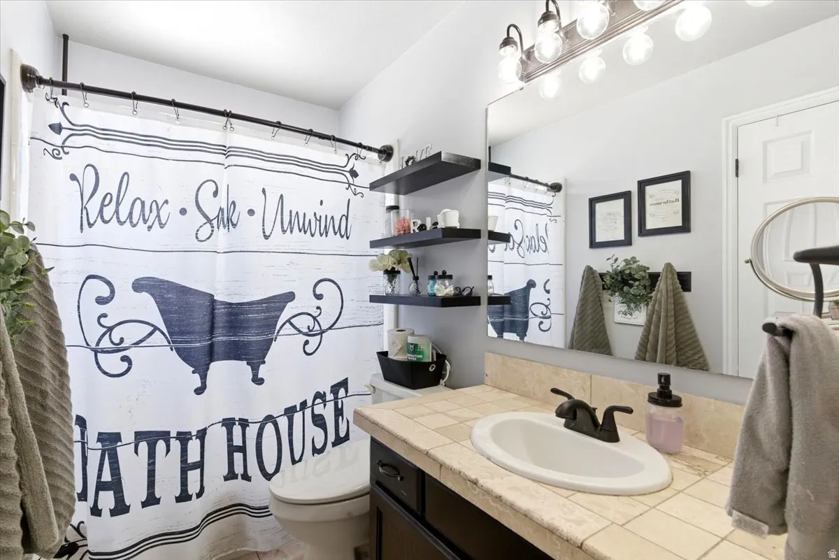 Bathroom featuring a vanity with a tile countertop, integrated sink, and an expansive wall mirror