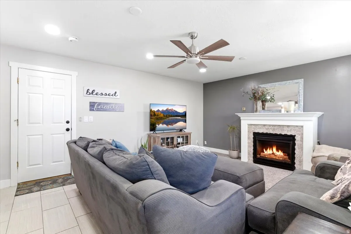 Living area featuring a fireplace with a white mantel and tile surround, light gray walls, a ceiling fan with integrated lighting, and wood-finish flooring