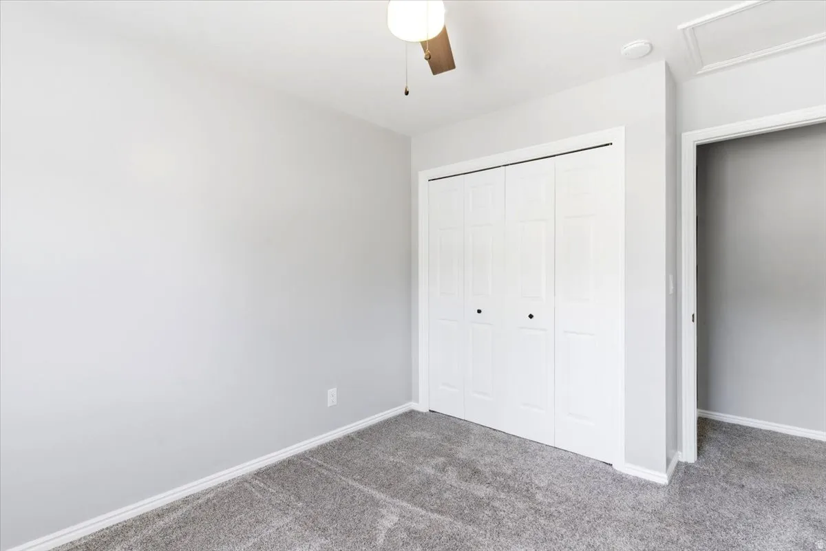 Carpeted interior room featuring a bi-fold closet, ceiling fan, and light gray wall paint