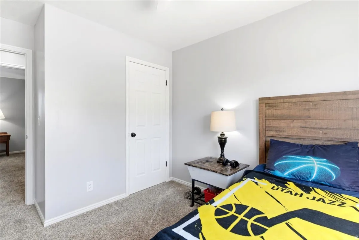 Carpeted room featuring a wood-finish headboard, light gray painted walls, a white paneled door with black hardware, and white baseboards