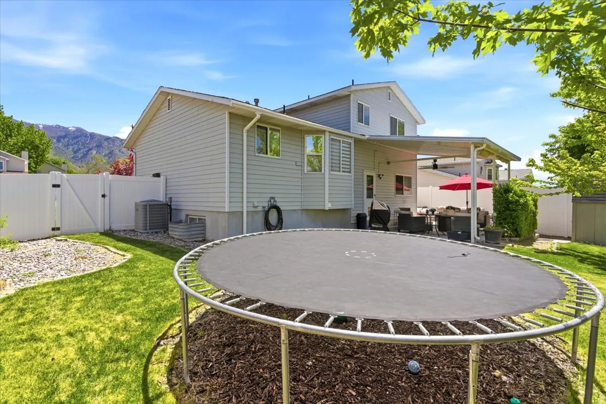 Spacious backyard featuring a covered patio, manicured lawn, and white privacy fencing