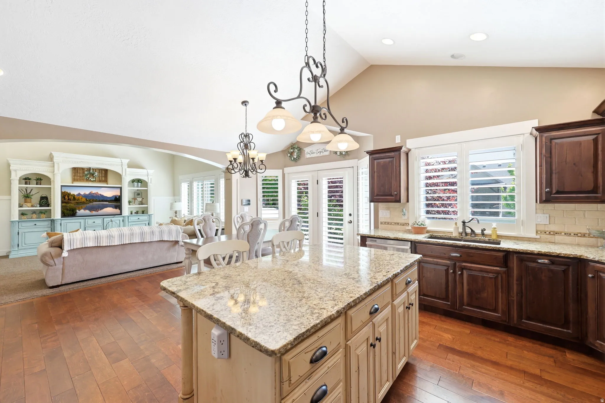 Expansive kitchen featuring a large central island with light cabinetry, granite countertops, wood-finish flooring, and dark wood perimeter cabinetry