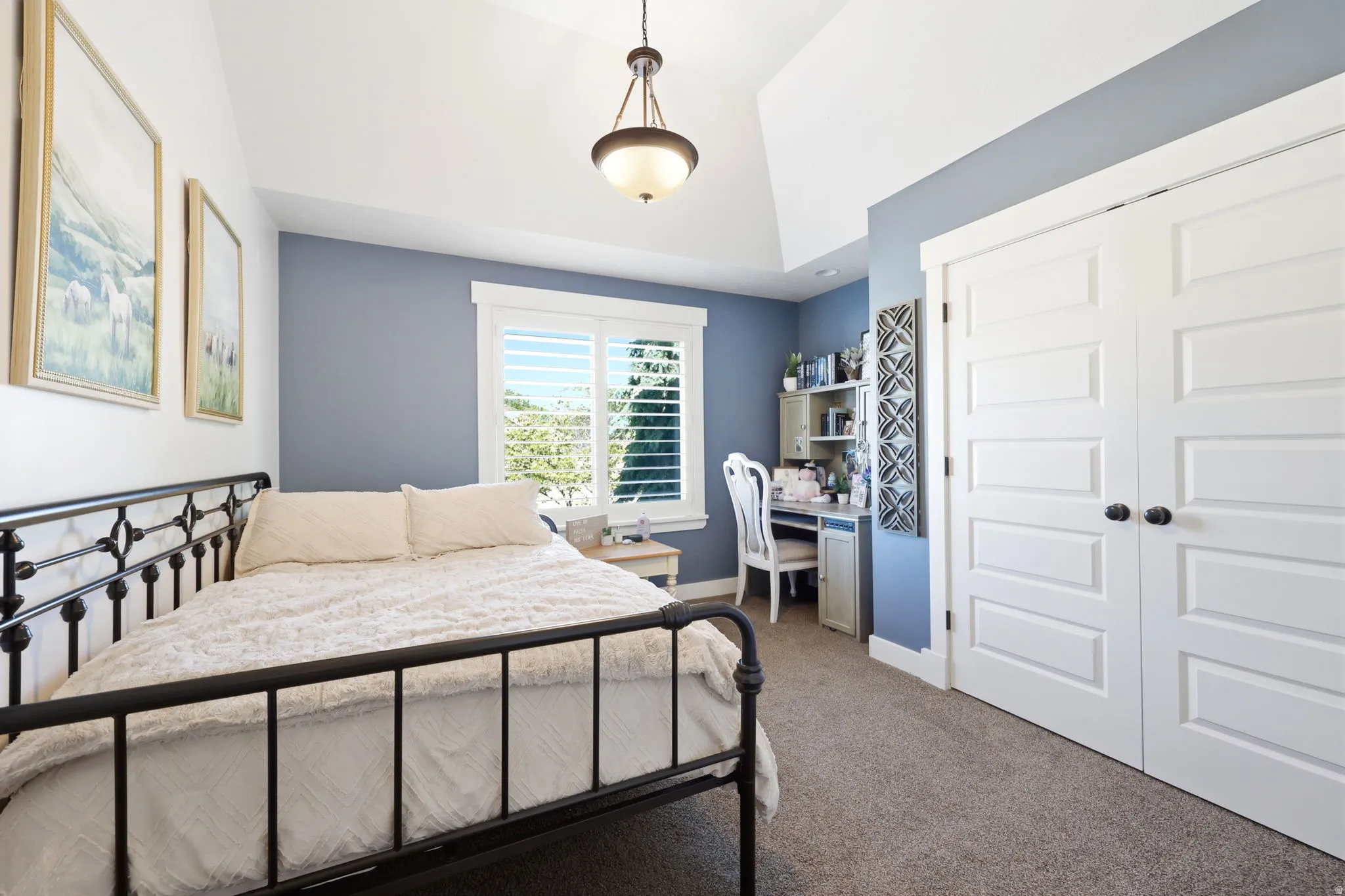 Bedroom featuring vaulted ceilings, a window with plantation shutters, a built-in desk, and double bifold closet doors