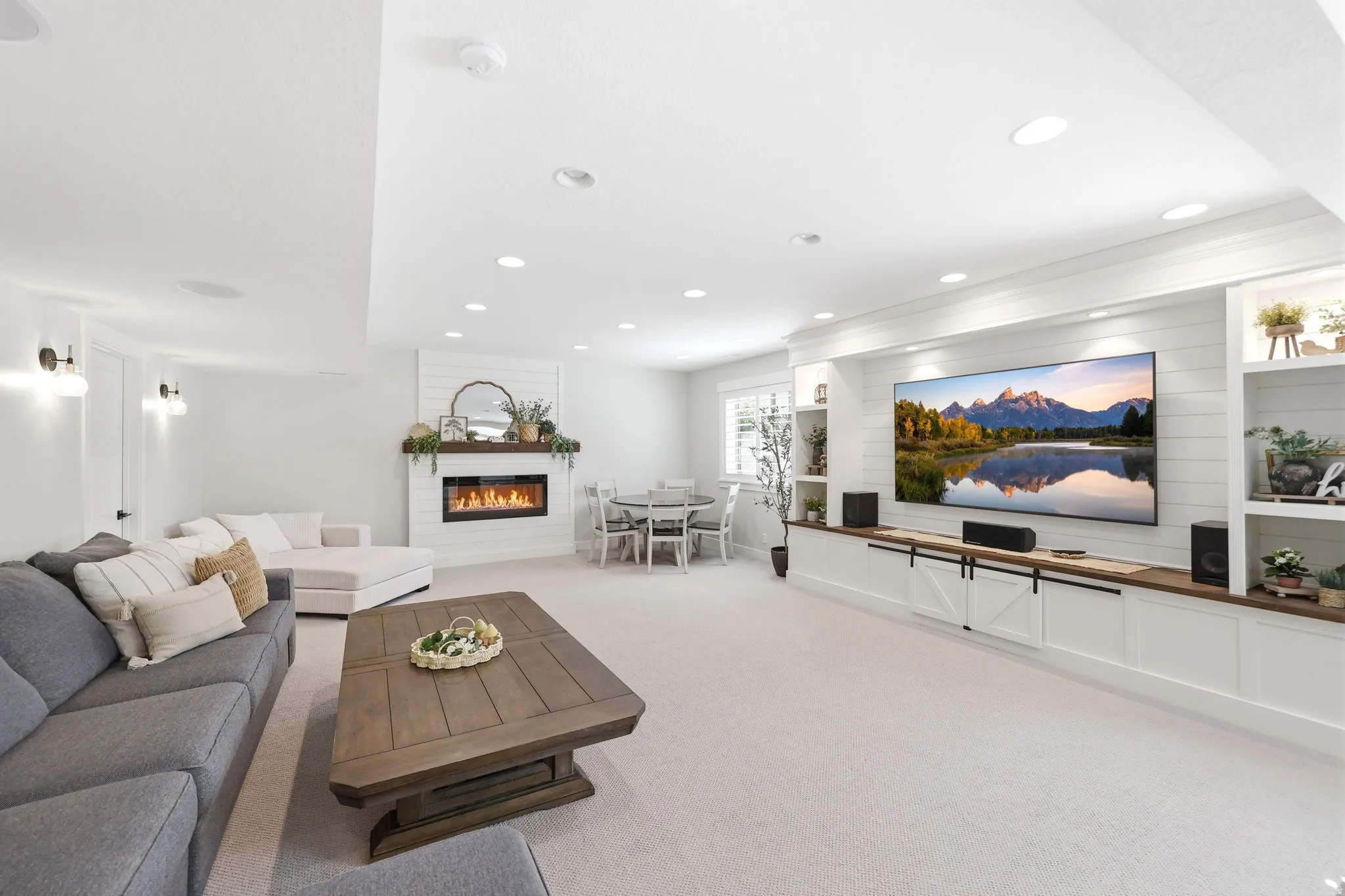 Spacious open-concept living area featuring a built-in entertainment center with shiplap accent wall, an electric fireplace with a wood mantel, recessed lighting, and soft carpeting