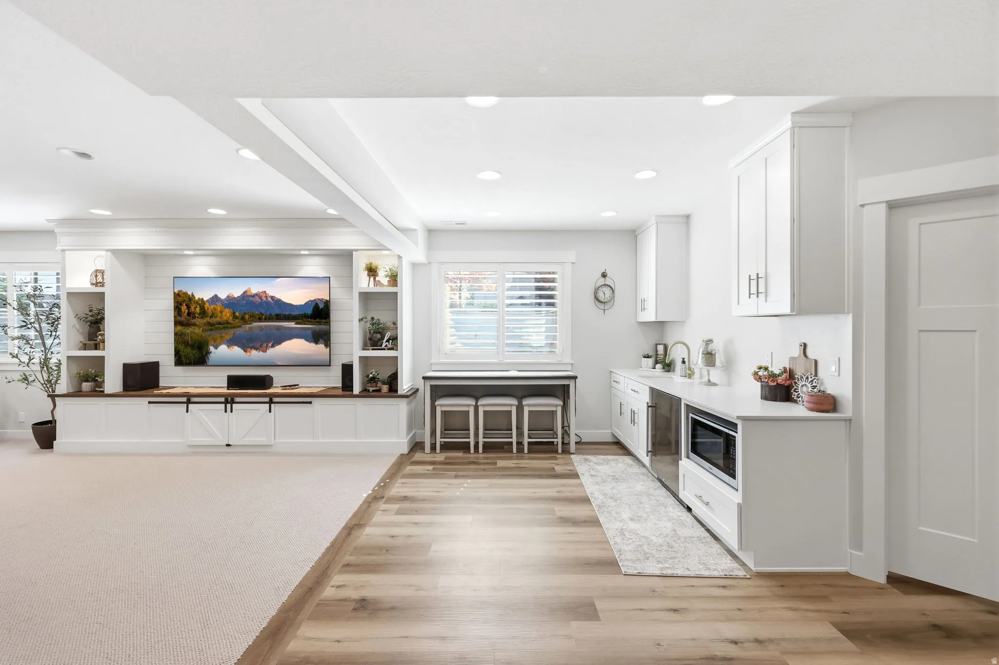 Open-concept living area featuring a built-in entertainment center with shiplap backing, a wet bar with white cabinetry and an integrated microwave, recessed lighting, and a blend of plush carpeting and wood-finish flooring
