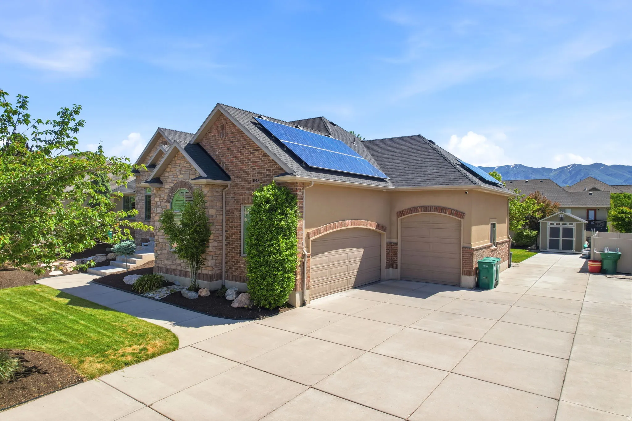 Exterior featuring brick and stucco finishes, a multi-car concrete driveway, solar panels, and a gabled roofline