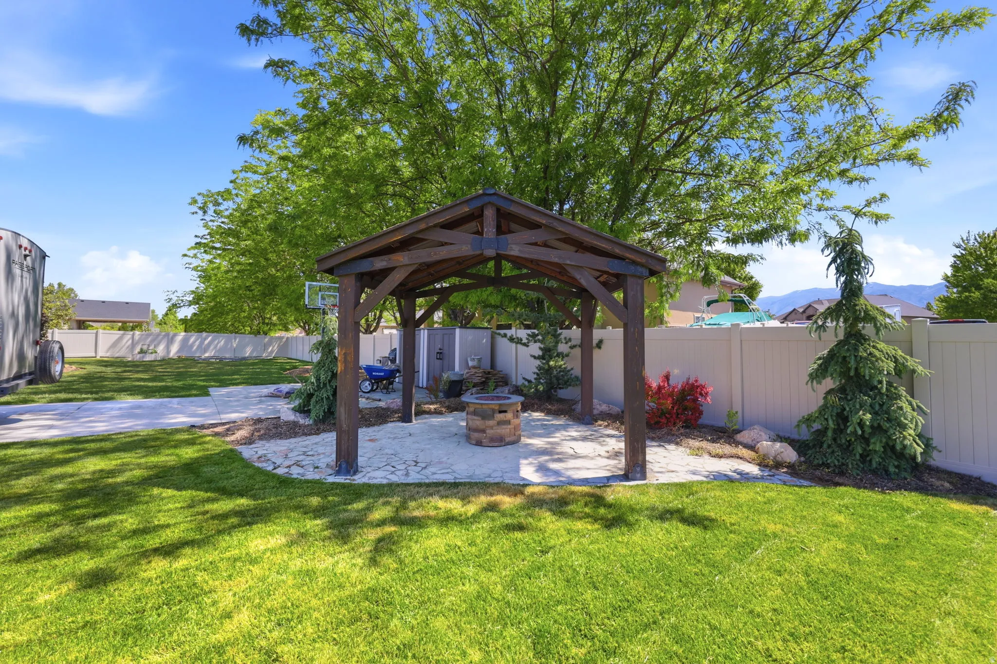 Spacious backyard featuring a stone patio with a wood-frame gazebo, a built-in stone fire pit, and a manicured lawn
