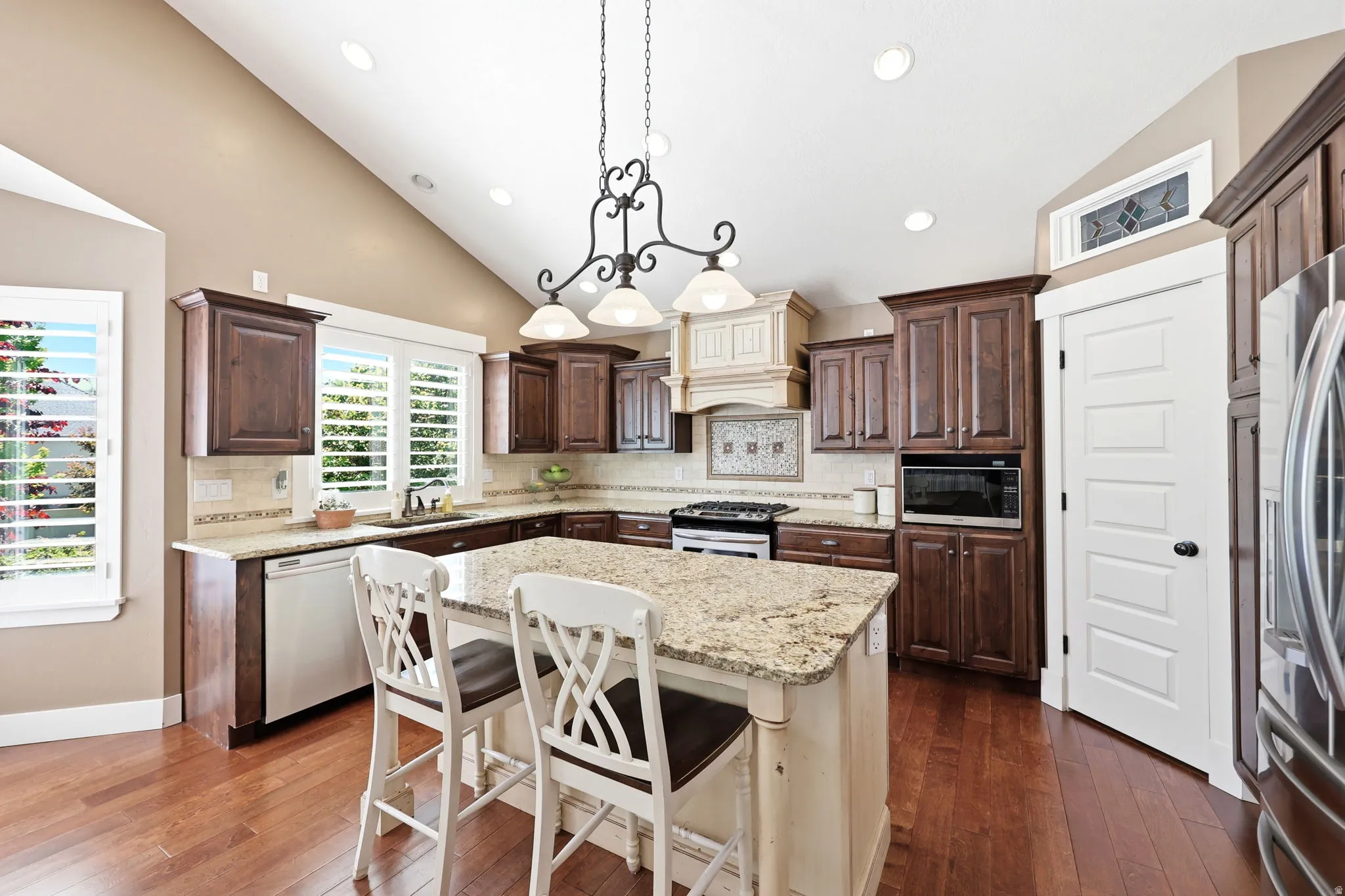 Spacious kitchen featuring an angled ceiling with recessed lighting, wood-finish flooring, dark wood cabinetry, a center island with a light-toned countertop, and white plantation shutters
