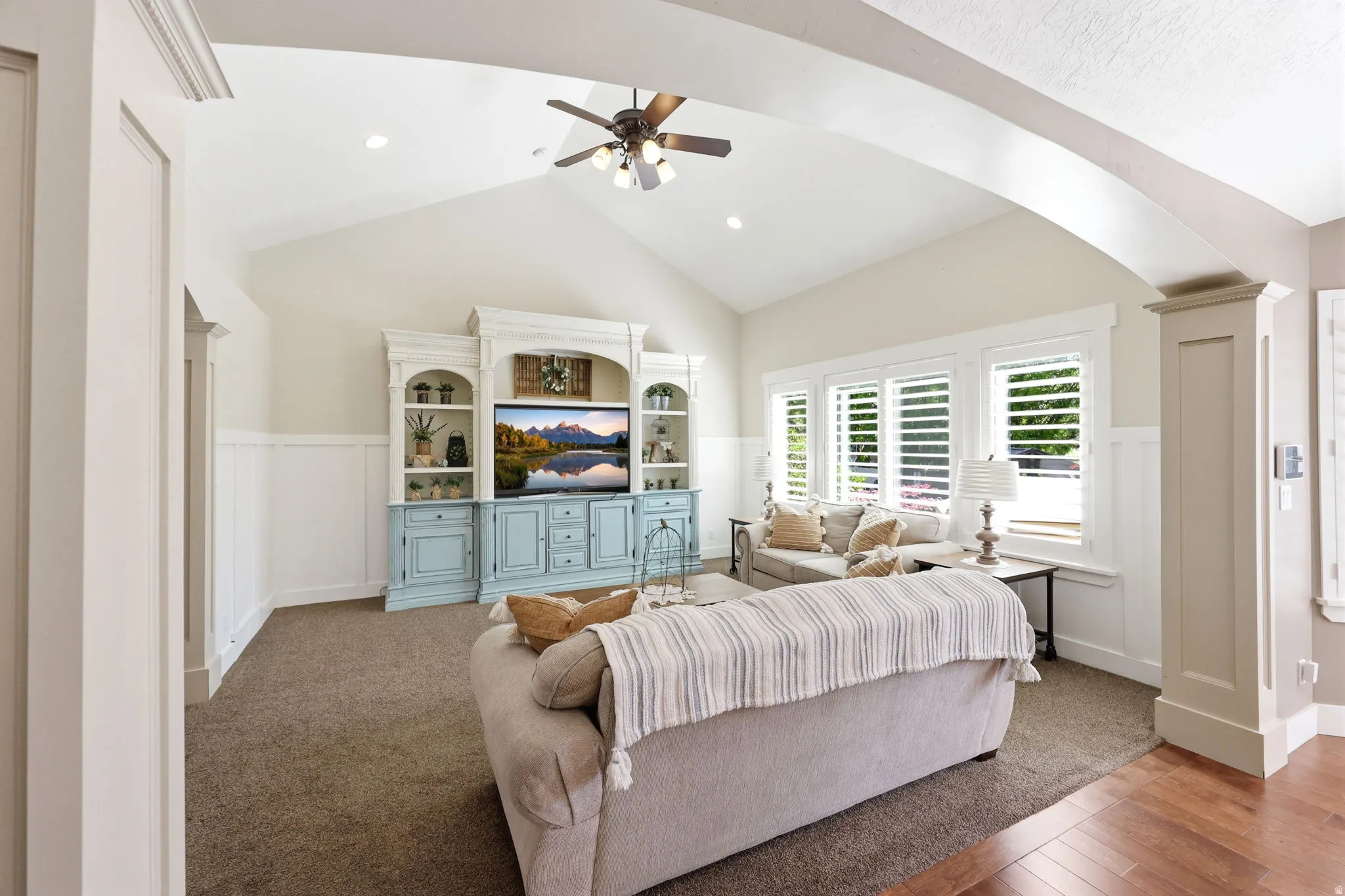 Vaulted ceiling with a ceiling fan, recessed lighting, white board and batten paneling, custom built-in entertainment center, and plantation shutters