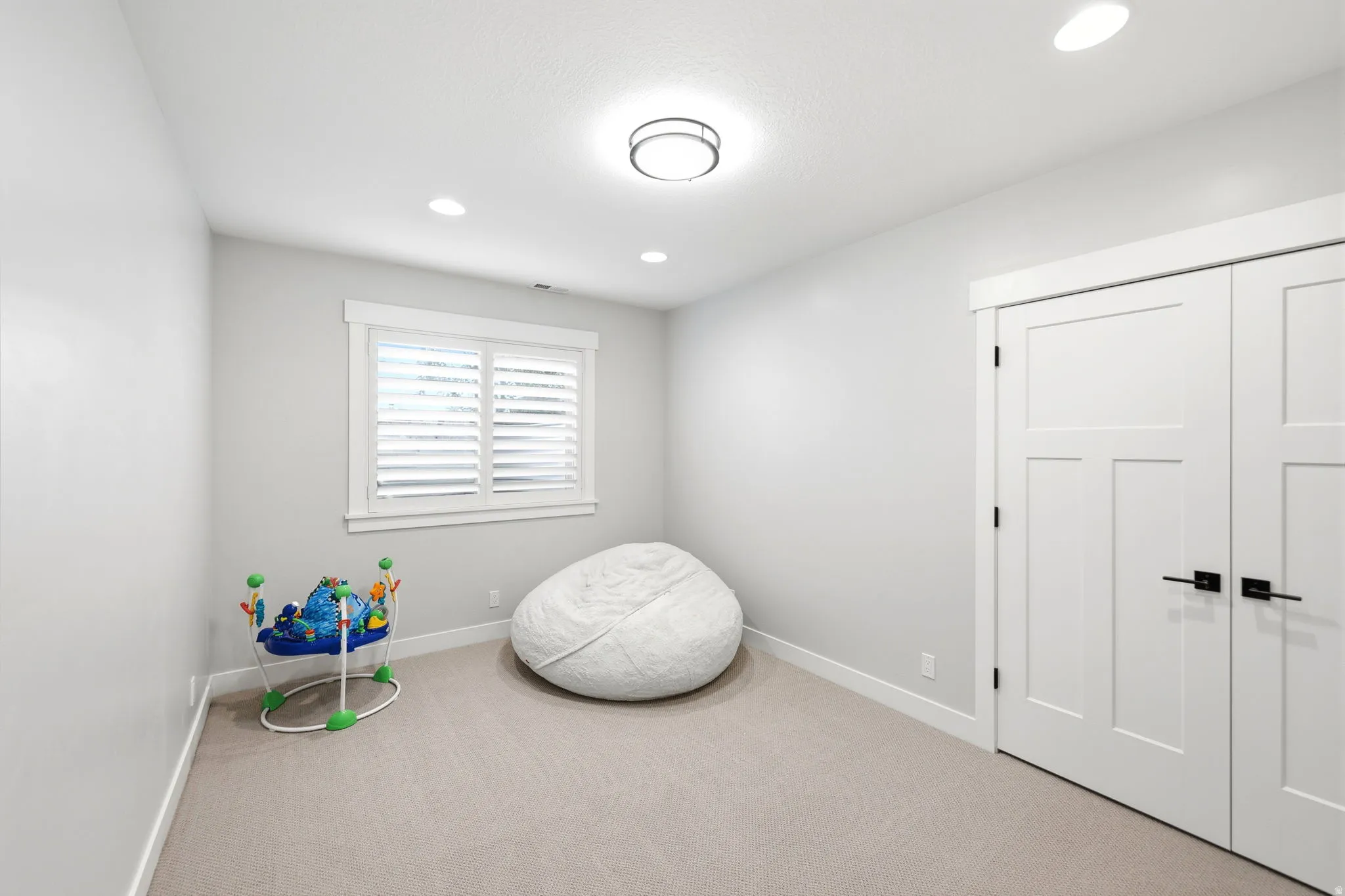 Carpeted room featuring white walls, a single window with white plantation shutters, and a closet with white paneled doors and black hardware
