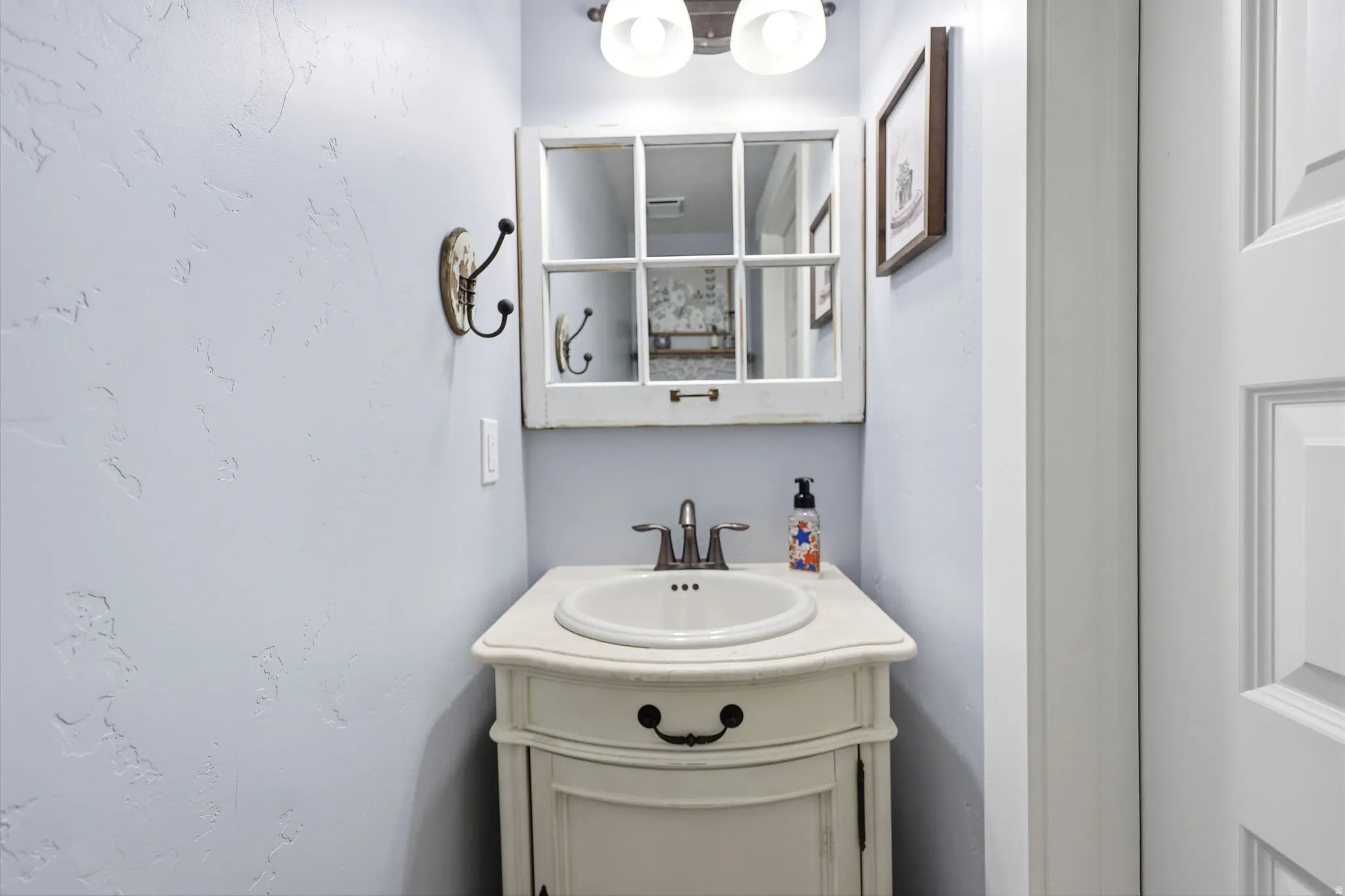 Powder room featuring a white single-sink vanity with a distressed finish, brass faucet, and a wall-mounted mirror with a windowpane design