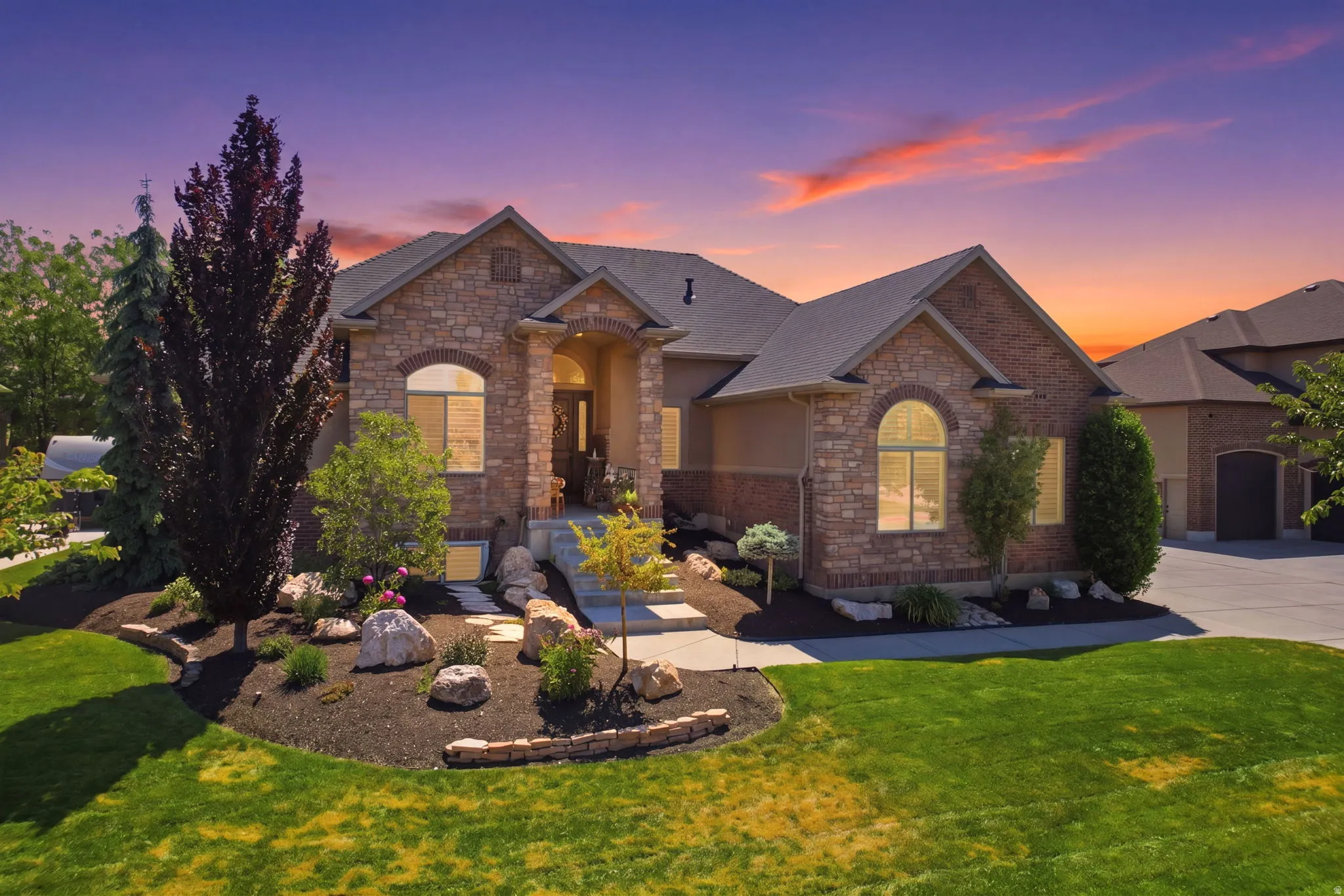 Stone and stucco exterior featuring a prominent arched entry, a multi-car driveway, mature landscaping with decorative rocks, and arched windows