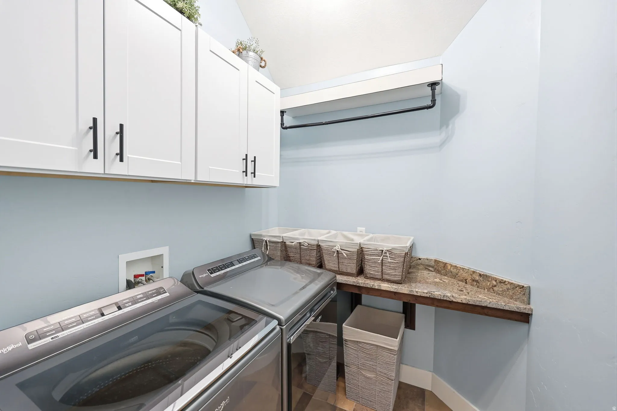 Laundry area featuring white shaker-style cabinetry with matte black hardware, a built-in hanging rod, a wood-finish countertop, and a granite-look backsplash
